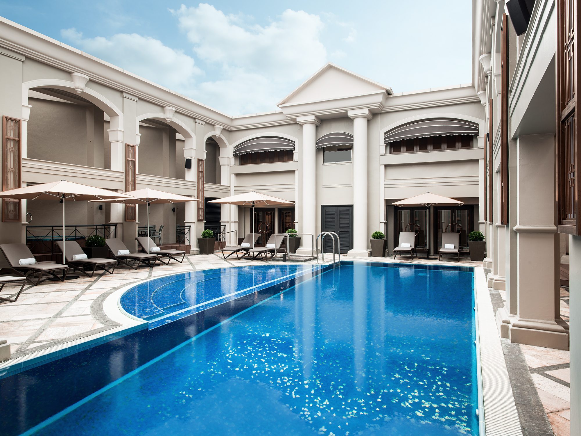 The colonnaded rooftop pool courtyard at The Langham Hong Kong, cream umbrellas and sun loungers around a blue tiled pool.