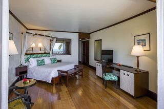 A hotel room with a bed, bedside table, lamp, desk, chair, and a TV.
