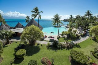 A resort with a swimming pool, palm trees, and thatched-roof huts.