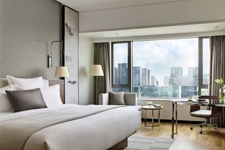 A modern hotel room with a large bed, a desk, and a view of the city skyline.