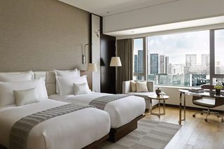 A hotel room with two beds, a desk, a chair, and a view of the cityscape.