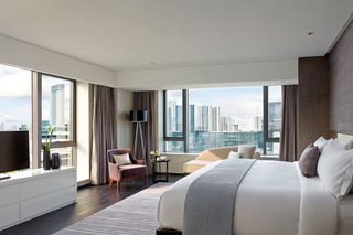 A modern hotel room with a large bed, a seating area, and a view of the cityscape.