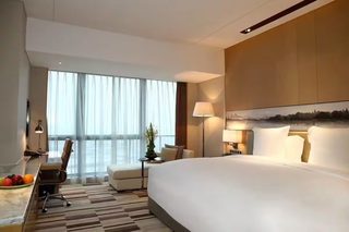 A hotel room with a large bed, a desk with a chair, a sofa, and a large window with curtains.