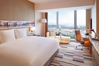 A modern hotel room with a large bed, a desk, a chair, and a view of the city.