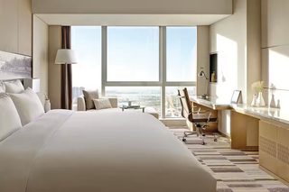 A modern hotel room with a large bed, a desk, and a view of the city.