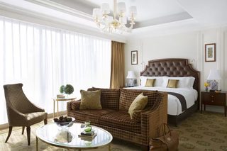 A hotel room with a large bed, a brown sofa, a glass coffee table, and a chair.