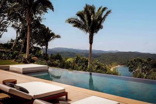 An infinity pool with lounge chairs, surrounded by palm trees and a view of a lake and mountains.