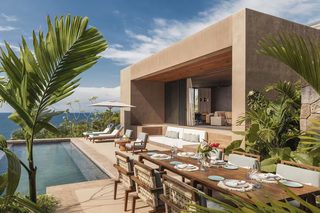 A modern outdoor dining area with a pool, lounge chairs, and a view of the ocean.