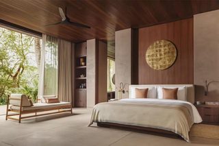 A modern bedroom with a large bed, a wooden ceiling fan, a built-in shelf with decorative items, and a view of greenery outside.