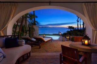 An outdoor seating area with a pool, lounge chairs, and a view of the ocean at dusk.