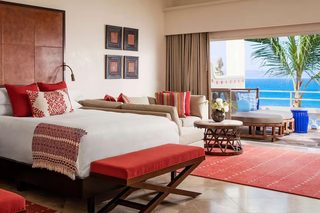 A hotel room with a bed, a bench, a table, and a view of the ocean.