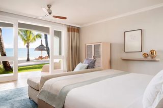 A hotel room with a bed, a ceiling fan, a view of the beach, and a window with curtains.