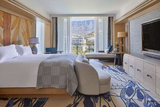A hotel room with a large bed, a sofa, a TV, a desk, and a view of mountains.