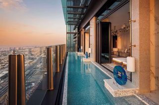 A rooftop infinity pool with a city view, a glass balustrade, and a seating area with a sofa and lamps.