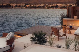 A waterfront patio with a pool, seating area, and a view of a cityscape and mountains.