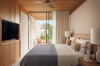 A modern hotel room with a large bed, a television, a nightstand with lamps, and a view of the outdoors.