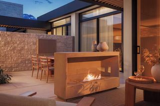 An outdoor patio with a stone wall, a fire feature, and a seating area with chairs and a table.