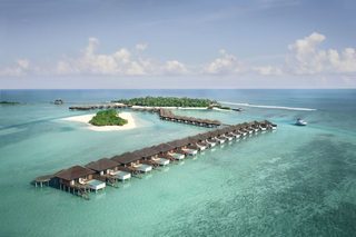 An overwater bungalows resort with multiple levels of accommodations extending into the turquoise sea, connected by walkways.