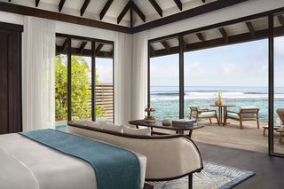 A bedroom with a large bed, a sofa, a small table with books, and a view of the ocean.