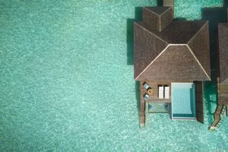 An overwater bungalow with a swimming pool, lounge area, and wooden deck.