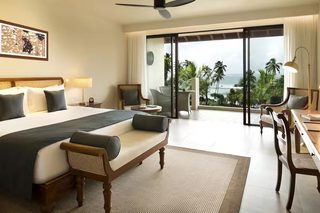 A hotel room with a large bed, a sofa, a dining table, and a view of the ocean.