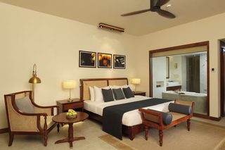 A hotel room with a bed, two chairs, a small table with fruit, a lamp, and artwork on the wall.