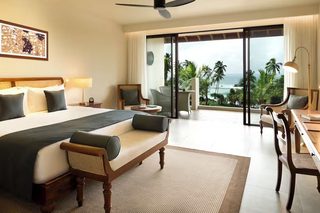 A hotel room with a large bed, a sofa, a dining table, and a view of the ocean.