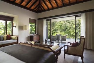 A bedroom with a large bed, a desk, a chair, and a view of the outdoors.