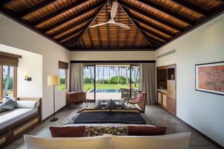 A spacious bedroom with a large bed, a ceiling fan, a view of the pool, and a seating area with a table and chairs.
