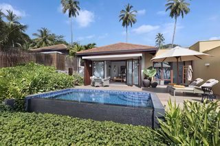 A poolside area with a lounge chair, a table, and a covered seating area.