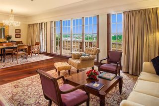 A spacious room with a large window, a chandelier, and a dining area with wooden furniture.