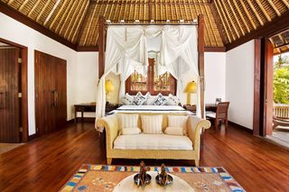 A spacious bedroom with a four-poster bed, wooden flooring, and a large window.