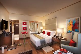 A hotel room with a large bed, a desk, a chair, a TV, a bathroom, and a painting on the wall.