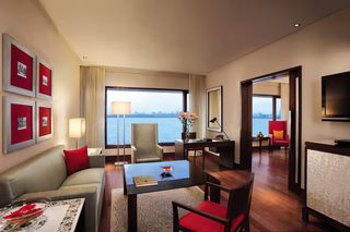 A hotel room with a sofa, a dining table, a TV, a desk, and a view of the water.