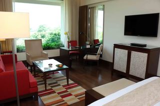 A hotel room with a sofa, armchairs, a small table with a vase and fruit, a TV, and a cabinet.