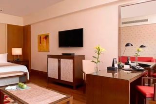 A hotel room with a bed, bedside tables, a desk with a chair, a television, and a mirror.