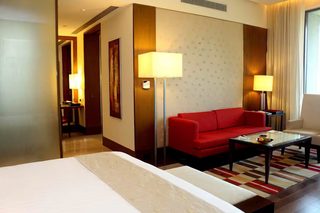 A hotel room with a bed, a red sofa, two lamps, and a coffee table.