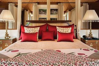A large bed with red and leopard print pillows, a floral bedspread, and wooden headboard. There are two bedside tables with lamps and a wooden dresser.
