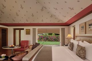 A hotel room with a bed, a chair, a small table, and a view of a garden.