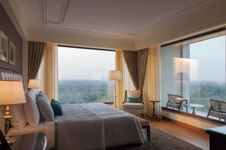 A hotel room with a large bed, two bedside tables, a chair, a small table, and a view of the outdoors.