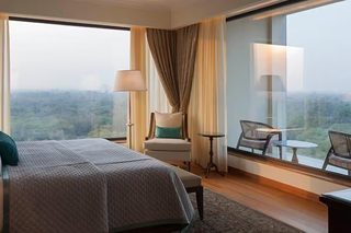 A hotel room with a large bed, a chair, a table, and a view of the city.