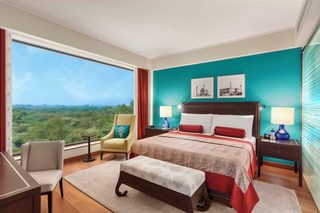 A hotel room with a large bed, two bedside tables, a desk, a chair, and a view of the outdoors.