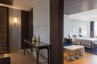 A modern hotel room with a large bed, a bedside table, and a decorative wall panel.