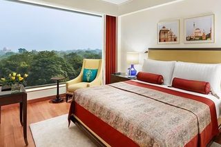 A hotel room with a large bed, a chair, a desk, and a view of the city.