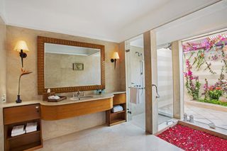 A bathroom with a large mirror, two sinks, a shower, and a glass door leading to a garden with flowers.