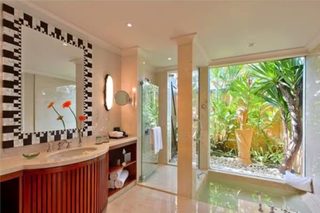 A modern bathroom with a large mirror, a sink, and a shower area. There is a view of greenery outside the window.