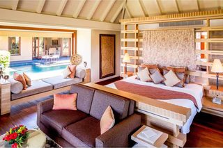 A bedroom with a bed, a sofa, a small table, a lamp, and a view of an outdoor swimming pool.
