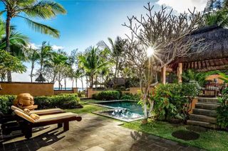 A tropical resort with a swimming pool, palm trees, and a thatched-roof structure.