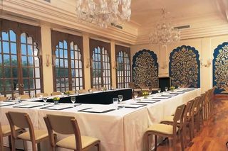 A long dining table with chairs, set for a meal, in a room with large windows and decorative wall panels.