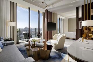 A modern hotel room with a sofa, armchair, coffee table, and a view of the cityscape.